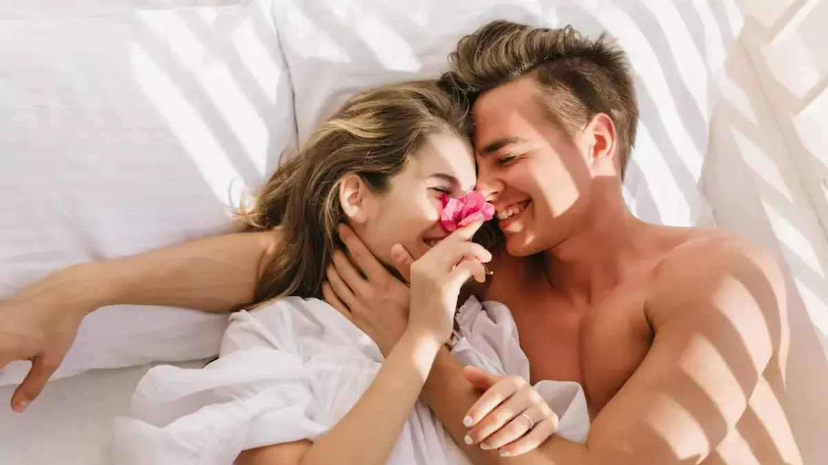 A couple lying face to face in bed in soft daylight, relaxed and smiling